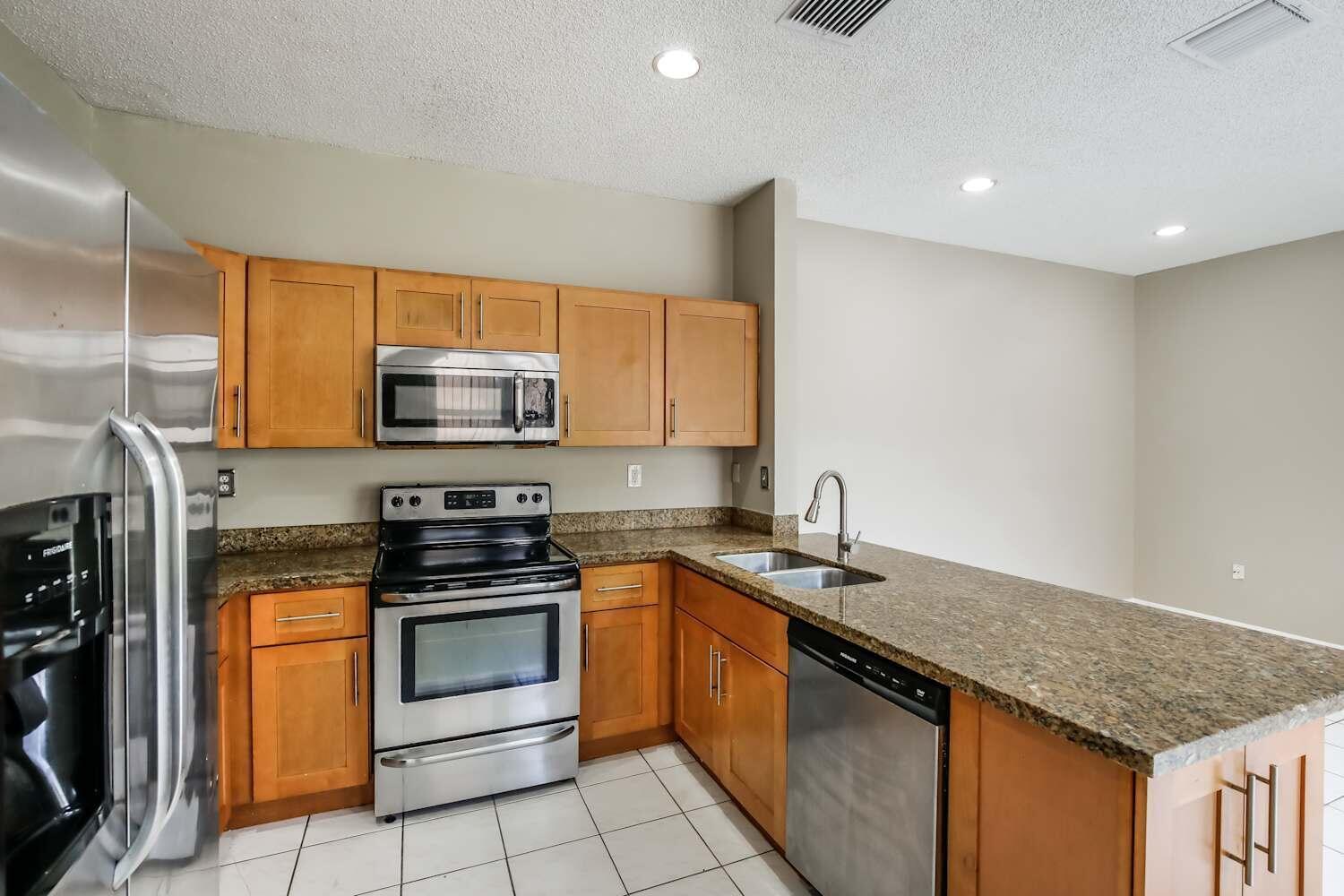 A kitchen features wood cabinets, granite countertops, stainless steel appliances, and white tile flooring — COOPER CITY, FL