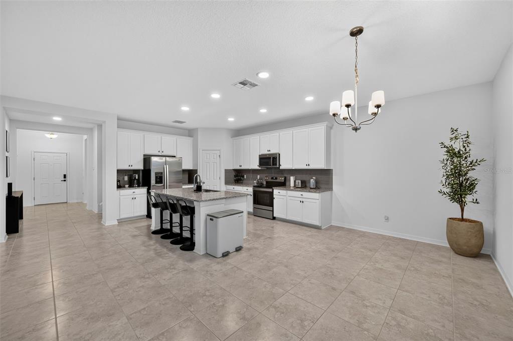 A bright kitchen features white cabinetry, a granite-topped island with bar stools, and tile flooring — 31903 SAPNA CHIME DRIVE, WESLEY CHAPEL, FL