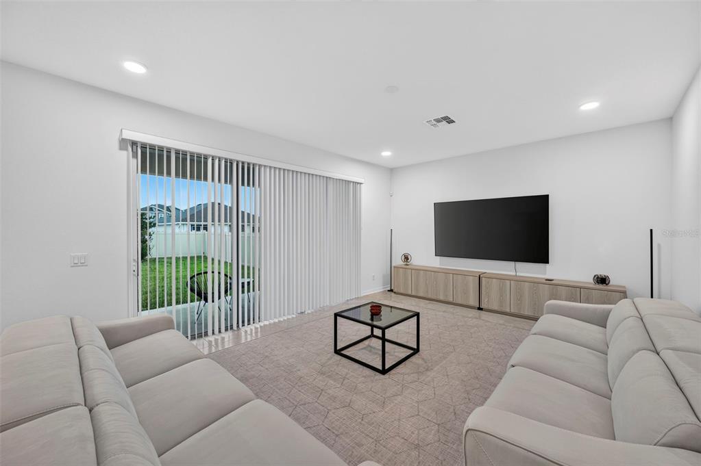 A living room features light-colored sofas, a glass coffee table, and a sliding glass door — 31903 SAPNA CHIME DRIVE, WESLEY CHAPEL, FL