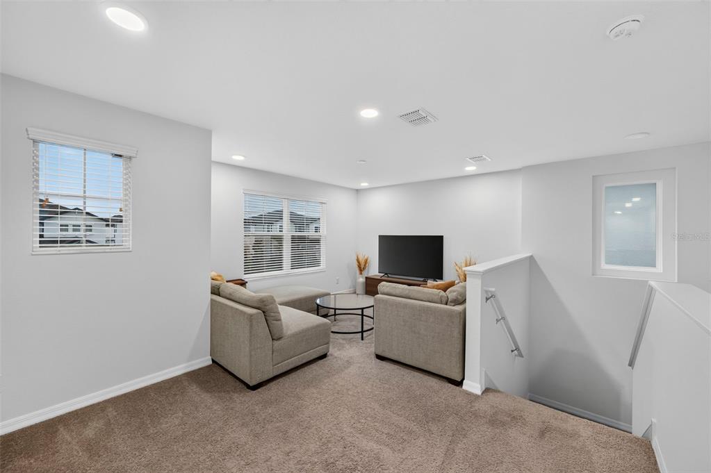 A carpeted loft area features a sectional sofa, a television, and a staircase with railing — 31903 SAPNA CHIME DRIVE, WESLEY CHAPEL, FL