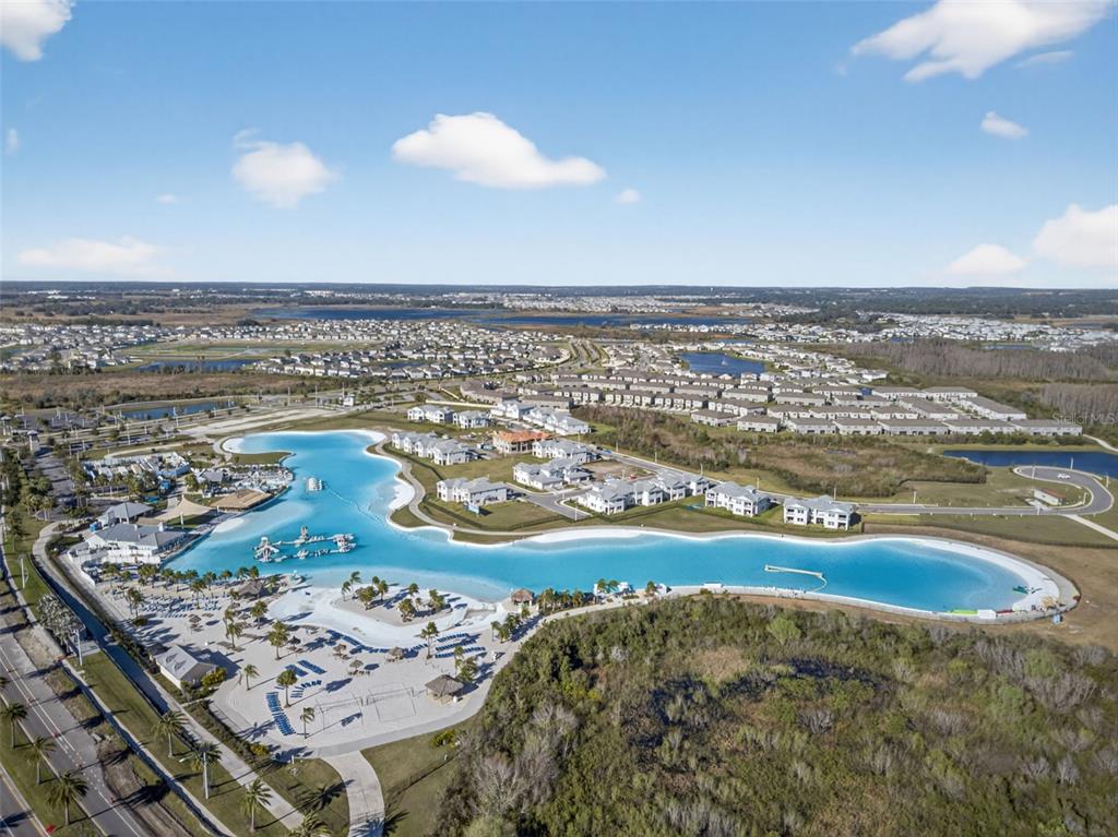 An aerial view shows a large man-made turquoise lagoon surrounded by residential buildings and landscaping — 31903 SAPNA CHIME DRIVE, WESLEY CHAPEL, FL