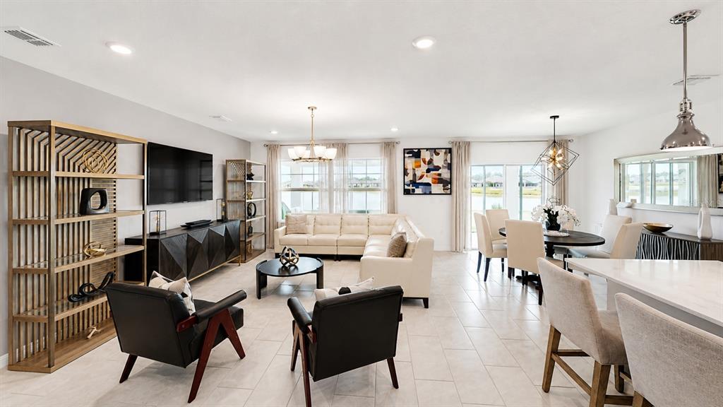 An open-concept living and dining area features light tile floors, neutral furniture, and large windows — 3884 CAPRI COAST DRIVE, PLANT CITY, FL