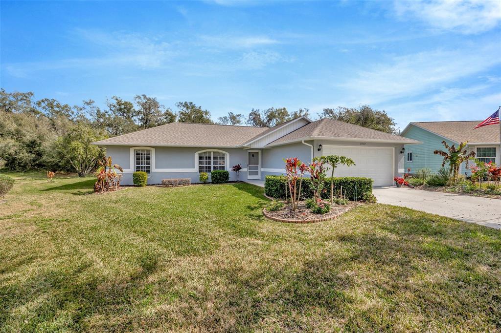 A single-story house with a gray exterior, a two-car garage, and a landscaped front yard — 37157 FOXRUN PLACE, ZEPHYRHILLS, FL