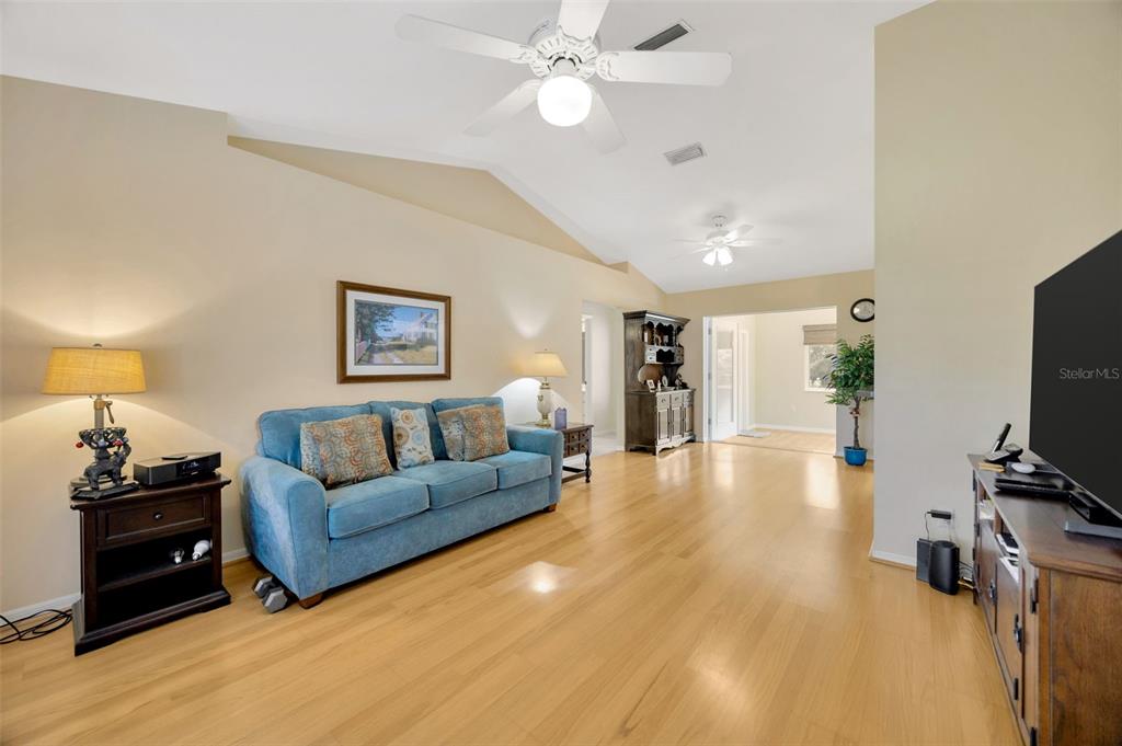 A living room features a blue sofa, hardwood floors, and a vaulted ceiling with fans — 37157 FOXRUN PLACE, ZEPHYRHILLS, FL