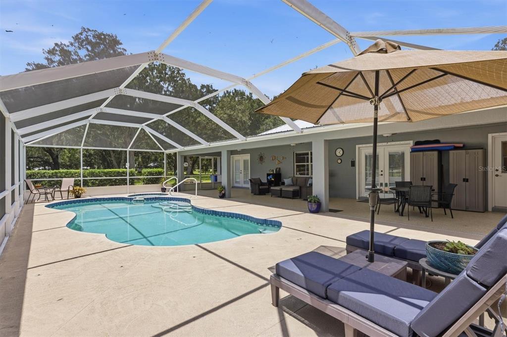 A screened-in pool patio features lounge chairs, an umbrella, and a view of the yard — 4917 SE BROWN ROAD, ARCADIA, FL