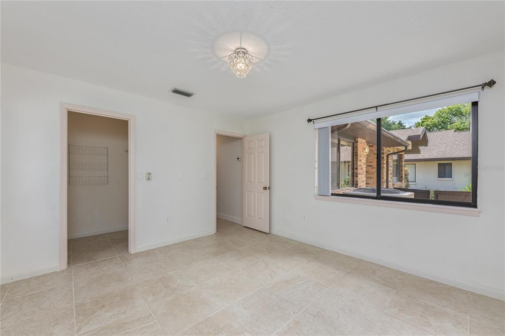 A bright bedroom features light tile flooring, white walls, a crystal light fixture, and windows — 109 WATERWOOD DRIVE, YALAHA, FL