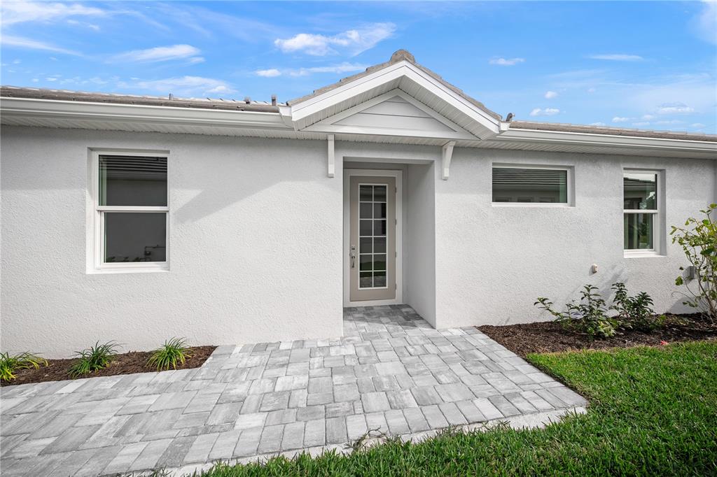 A white stucco house exterior features a paved walkway leading to a glass-paneled front door — 9533 LUNAR DOVE DRIVE, SARASOTA, FL