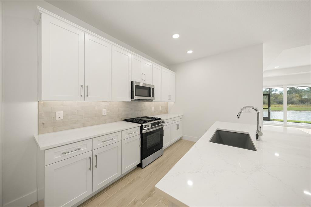 A modern kitchen features white cabinetry, quartz countertops, a stainless steel stove, and an island — 9533 LUNAR DOVE DRIVE, SARASOTA, FL