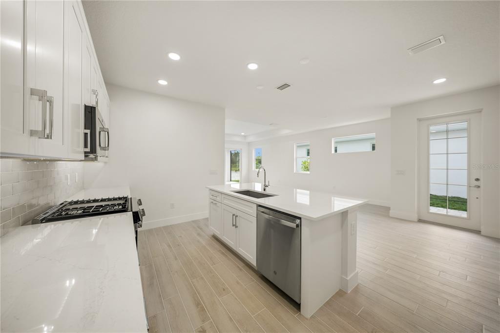 A modern kitchen features white cabinets, quartz countertops, a center island, and light wood-look flooring — 9533 LUNAR DOVE DRIVE, SARASOTA, FL