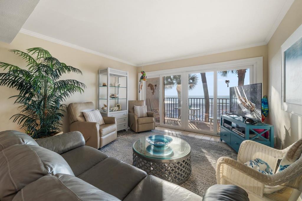 A living room with a leather sofa, armchairs, glass coffee table, and sliding doors to a balcony — 60 GULF BOULEVARD UNIT 201, INDIAN ROCKS BEACH, FL