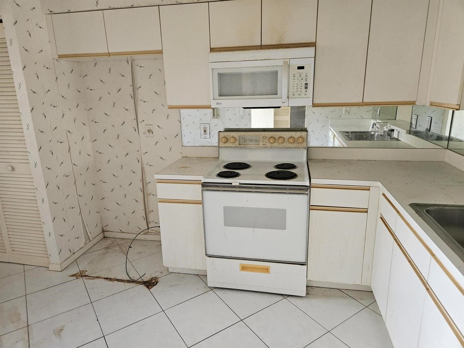 A dated kitchen features white cabinets, a white electric stove, and patterned wallpaper — 6065 Pointe Regal Circle # 105, Delray Beach FL 33484, DELRAY BEACH, FL