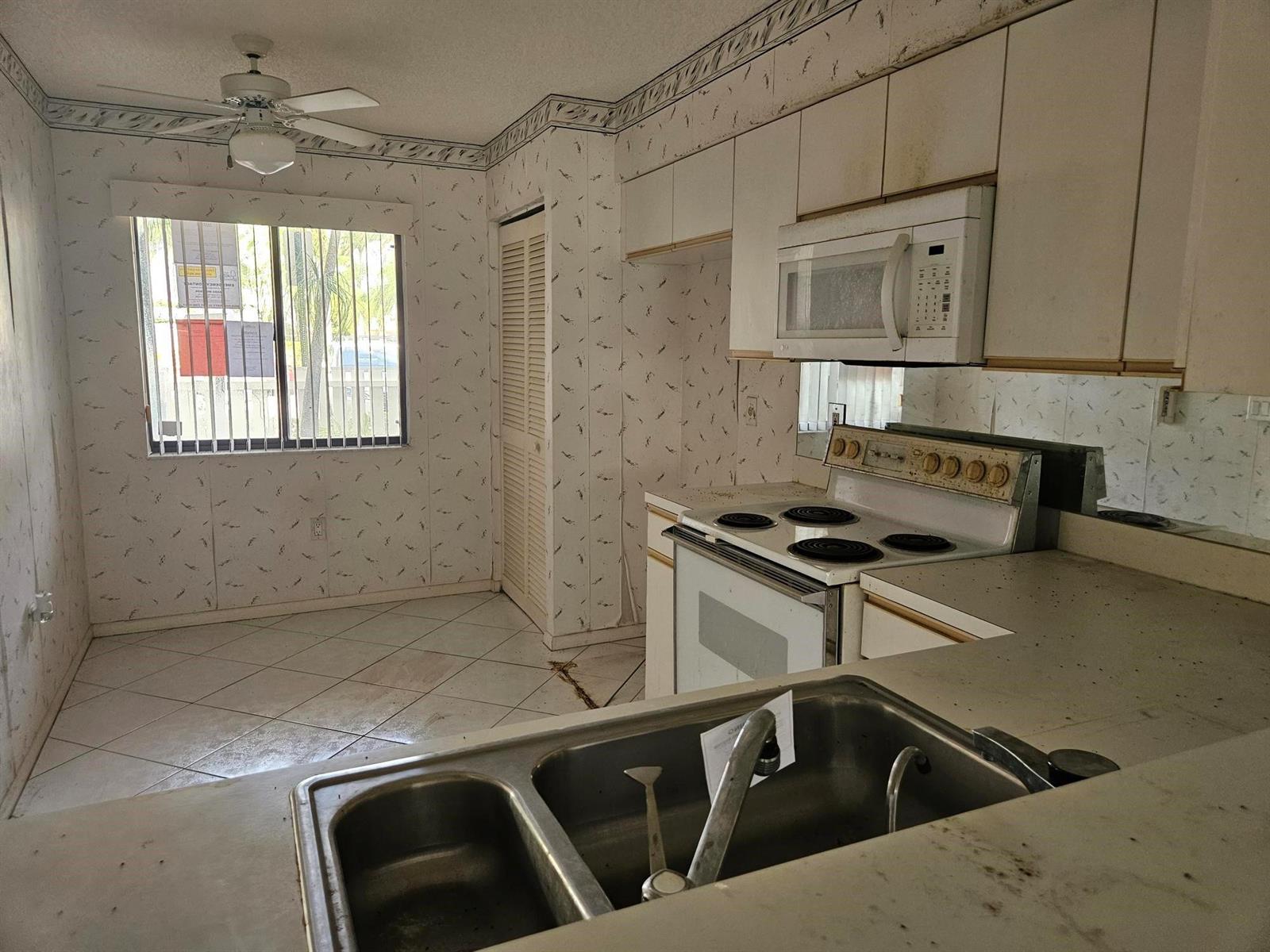 A kitchen with white cabinets, a double sink, an electric stove, and patterned wallpaper — 6065 Pointe Regal Circle # 105, Delray Beach FL 33484, DELRAY BEACH, FL
