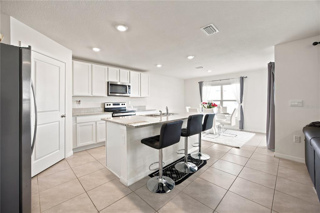 A kitchen features white cabinets, granite countertops, a center island with bar stools, and tile flooring — 8709 SW 46TH AVENUE, OCALA, FL