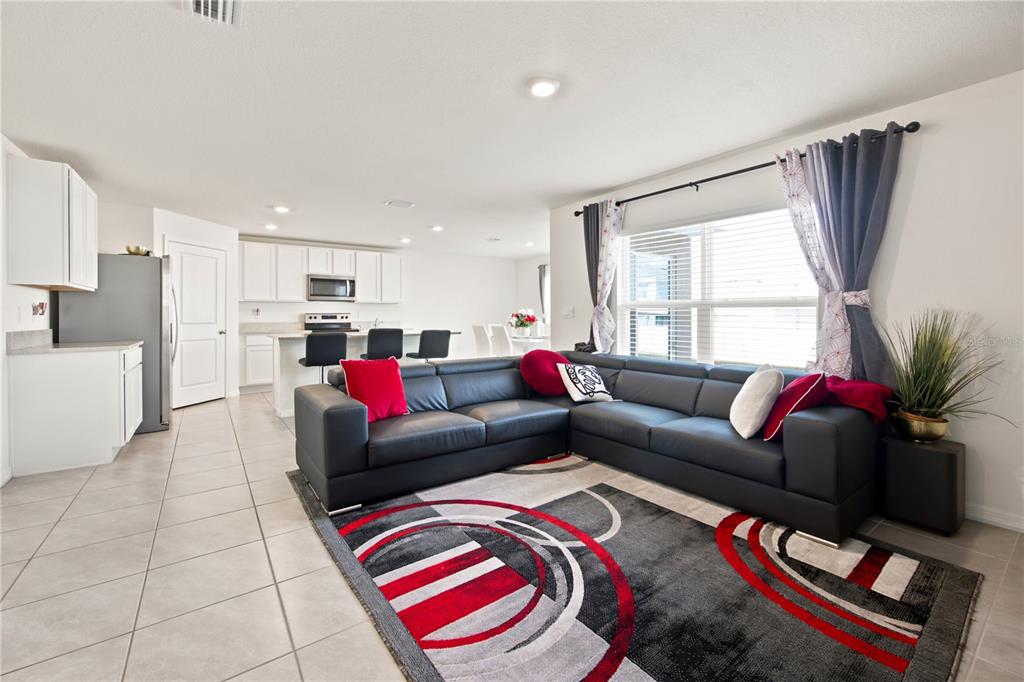 An open-concept living room features a black sectional sofa, a patterned rug, and a kitchen — 8709 SW 46TH AVENUE, OCALA, FL