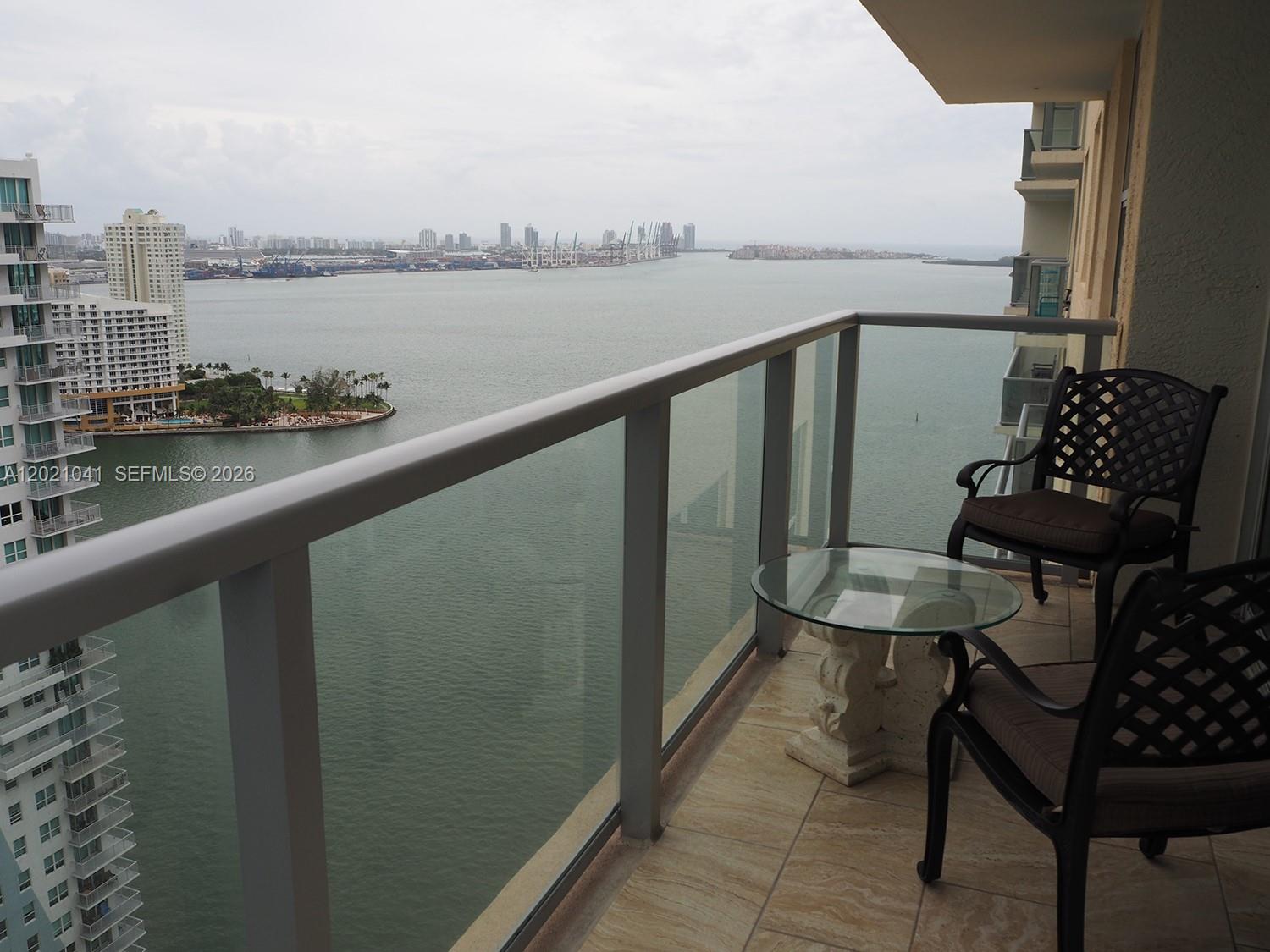 A balcony with two chairs and a glass table overlooks a bay and city skyline — 1155 BRICKELL BAY DR # 3102, Miami FL 33131, MIAMI, FL