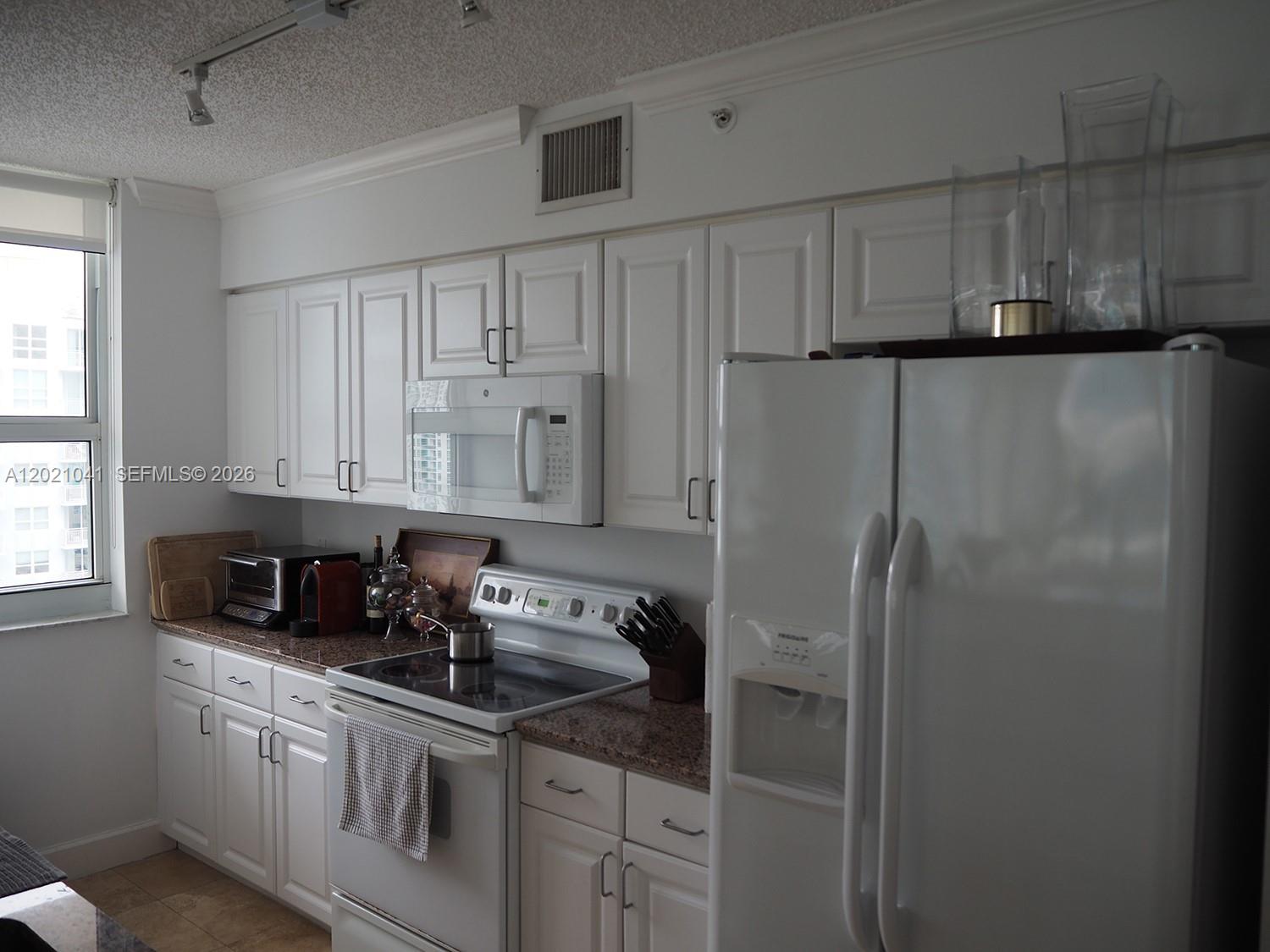 A kitchen features white cabinets, white appliances, and granite countertops — 1155 BRICKELL BAY DR # 3102, Miami FL 33131, MIAMI, FL