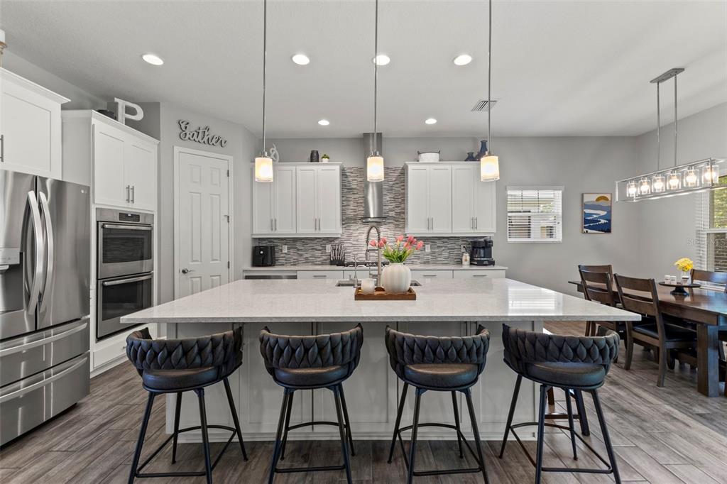 A modern kitchen features a large quartz island, white cabinetry, stainless steel appliances, and barstools — 6334 KNOB TREE DRIVE, LITHIA, FL