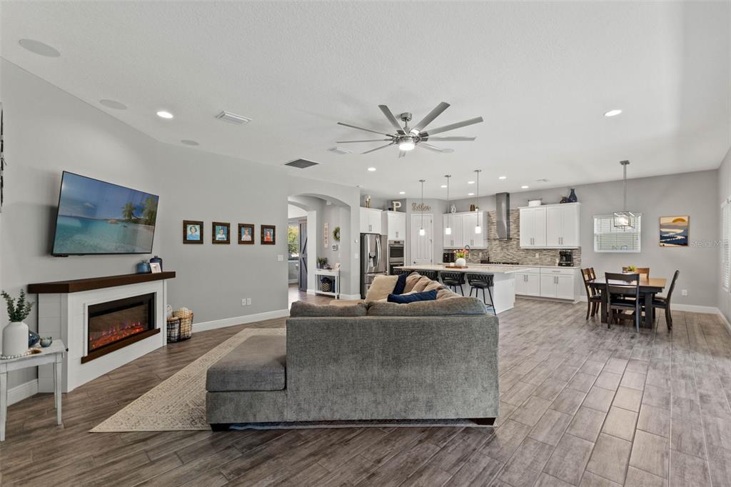 An open-concept living room and kitchen featuring a fireplace, gray sofa, and wood-look tile flooring — 6334 KNOB TREE DRIVE, LITHIA, FL