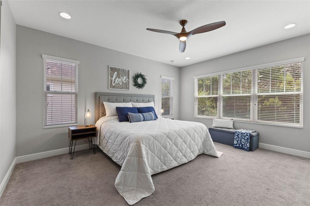 A bedroom features a gray upholstered bed, blue accent pillows, and a ceiling fan — 6334 KNOB TREE DRIVE, LITHIA, FL