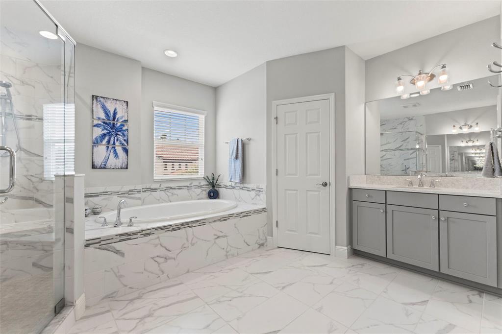 A bathroom features a soaking tub, a glass-enclosed shower, and a gray vanity with marble — 6334 KNOB TREE DRIVE, LITHIA, FL