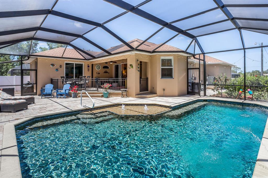 A swimming pool with a sun shelf sits inside a screened-in patio behind a house — 139 CREVALLE ROAD, ROTONDA WEST, FL