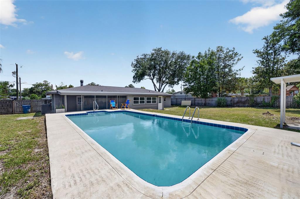 A rectangular swimming pool sits in the backyard of a single-story house with a patio — 577 PARKDALE COURT, DELAND, FL