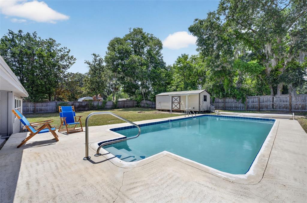 A backyard features a rectangular swimming pool with a metal handrail and two blue chairs — 577 PARKDALE COURT, DELAND, FL