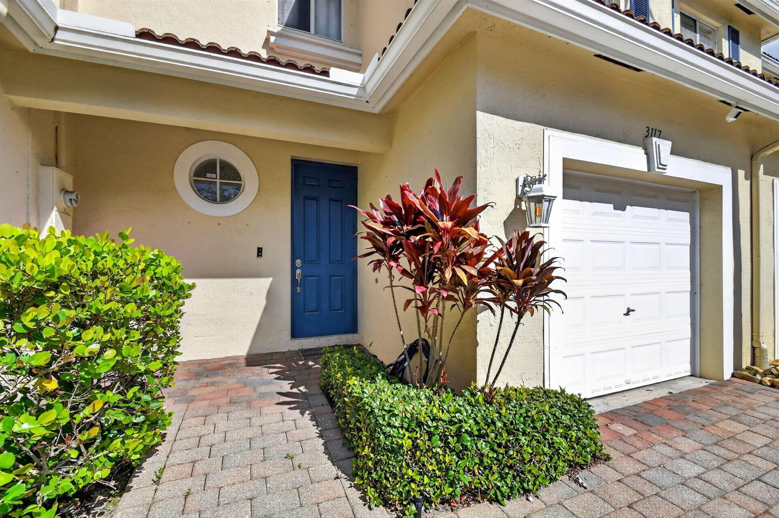 A blue front door and white garage door are set in a beige stucco exterior — 3117 N Evergreen Circle, Boynton Beach FL 33426, BOYNTON BEACH, FL