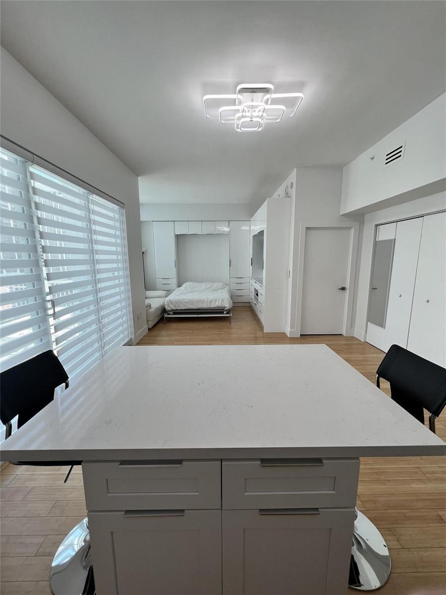 A modern studio apartment features a white kitchen island, a Murphy bed, and light flooring — 133 NE 2nd Avenue, Miami FL 33132, MIAMI, FL