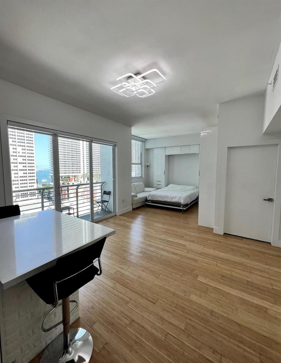 A studio apartment with a Murphy bed, light wood floors, and a balcony overlooking buildings — 133 NE 2nd Avenue, Miami FL 33132, MIAMI, FL