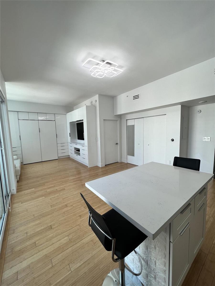A modern kitchen features a white quartz island, light wood flooring, and built-in cabinetry — 133 NE 2nd Avenue, Miami FL 33132, MIAMI, FL