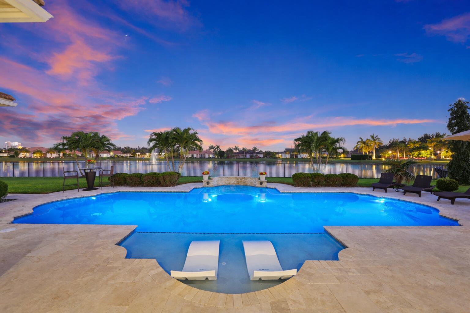 A backyard swimming pool with a tanning ledge and lounge chairs overlooks a lake at sunset — 5700 N Sterling Ranch Drive, Davie FL 33314, DAVIE, FL