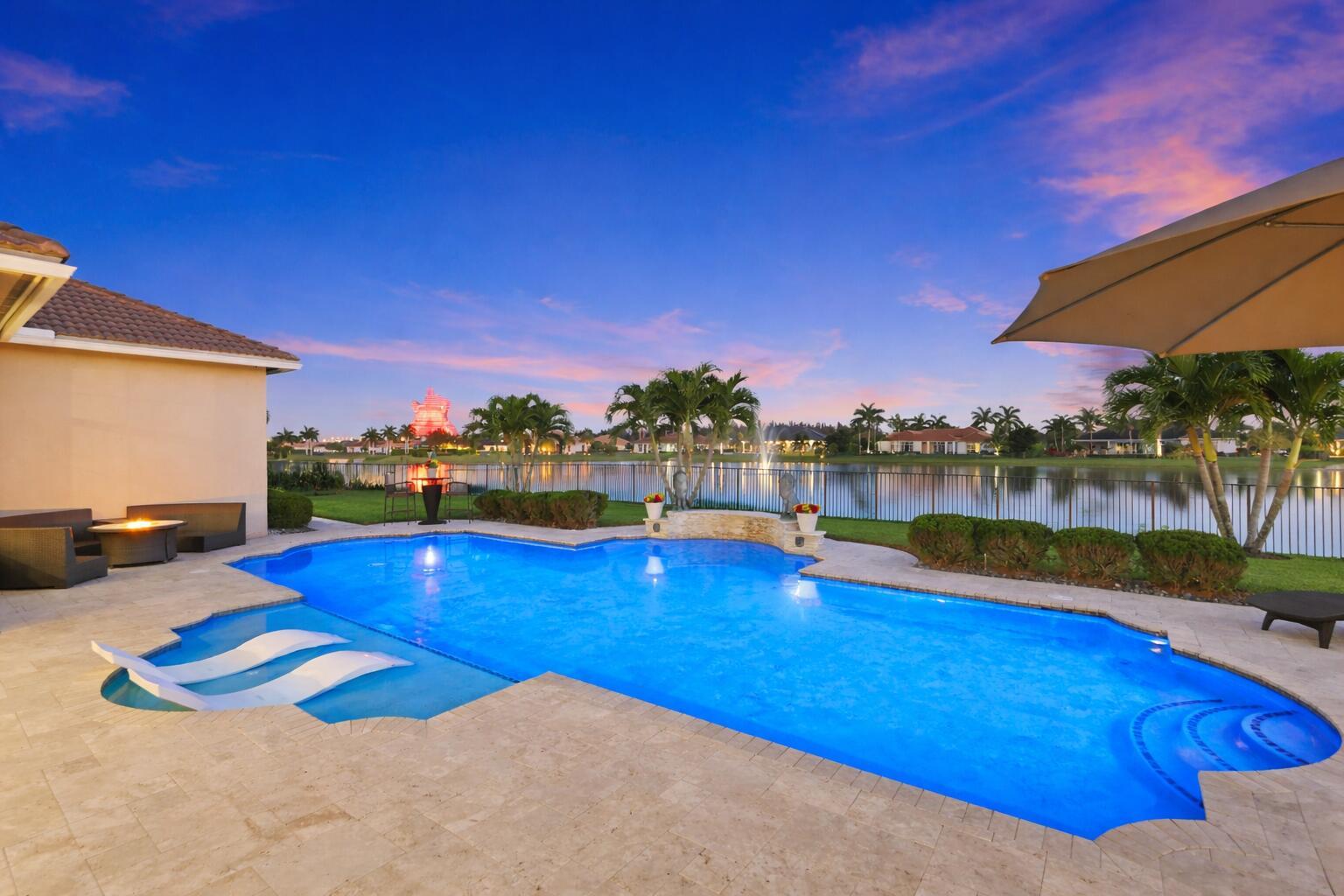 A swimming pool with lounge chairs sits on a stone patio overlooking a lake — 5700 N Sterling Ranch Drive, Davie FL 33314, DAVIE, FL
