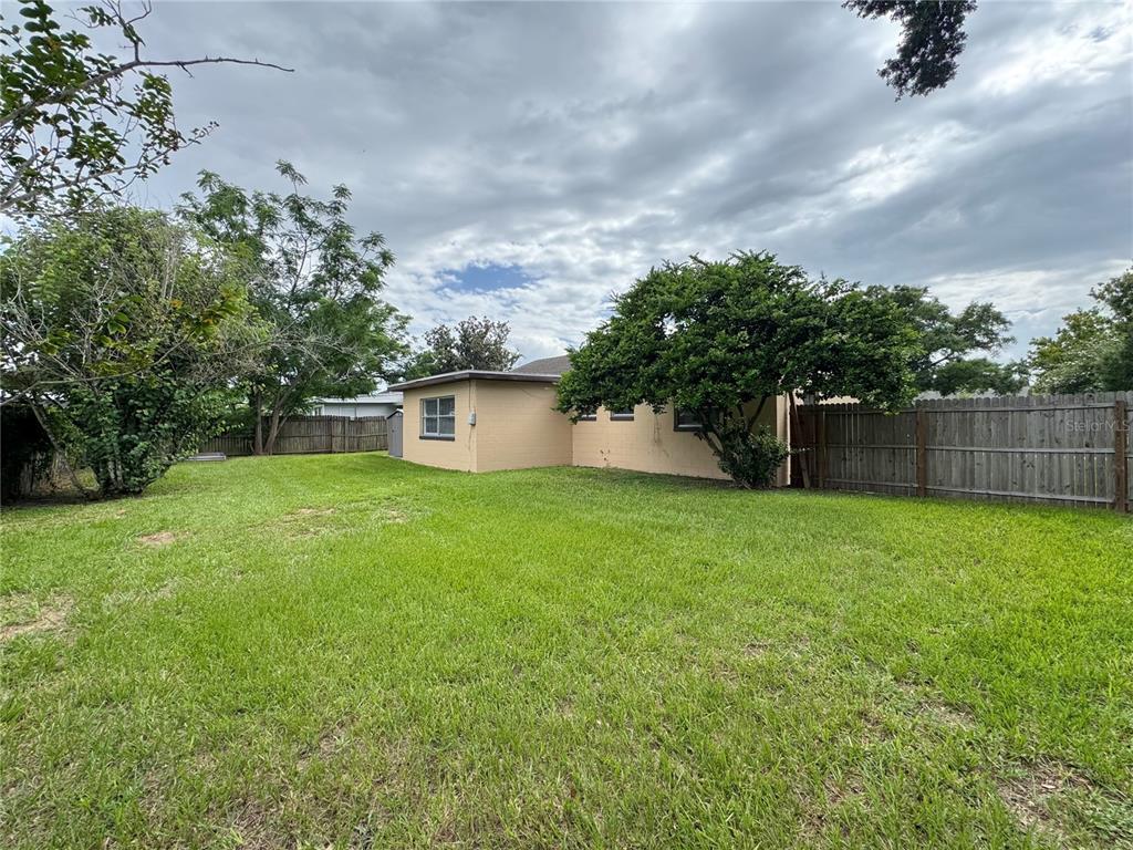 The exterior of a tan house with a grassy backyard and a wooden fence — 506 THOMAS AVENUE, WINTER HAVEN, FL