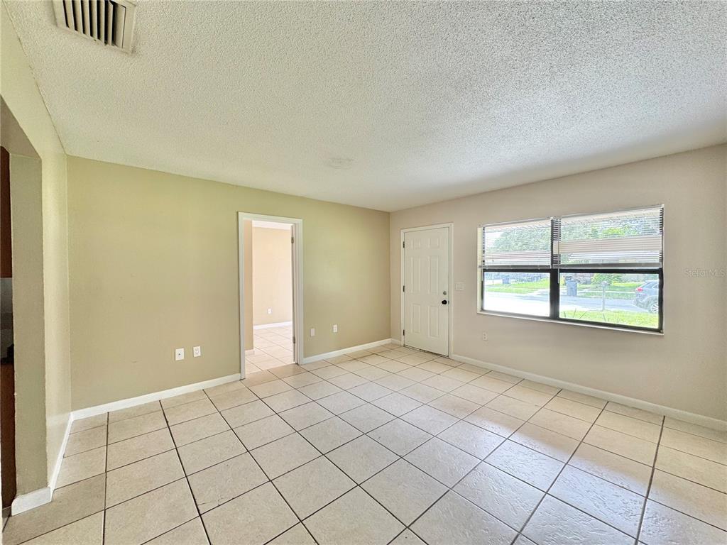An empty room with beige walls, white tile flooring, a window, and a white door — 506 THOMAS AVENUE, WINTER HAVEN, FL