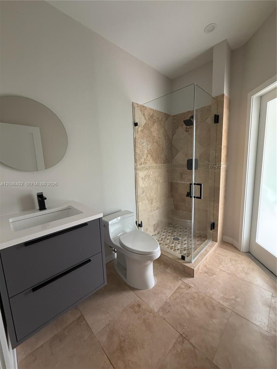 A modern bathroom features a gray vanity, a toilet, and a glass-enclosed stone shower — MIAMI, FL
