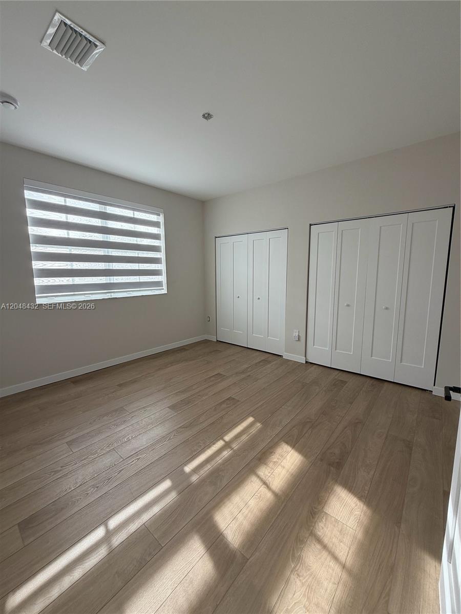 A bedroom features light wood-look flooring, two sets of white closet doors, and a window — MIAMI, FL