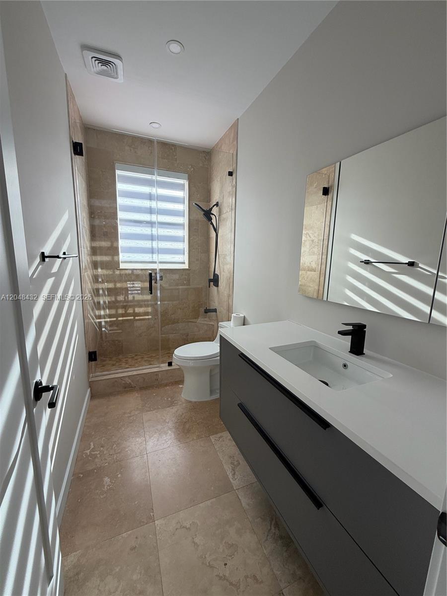 A modern bathroom features a gray vanity, a glass-enclosed shower, and beige tile flooring — MIAMI, FL