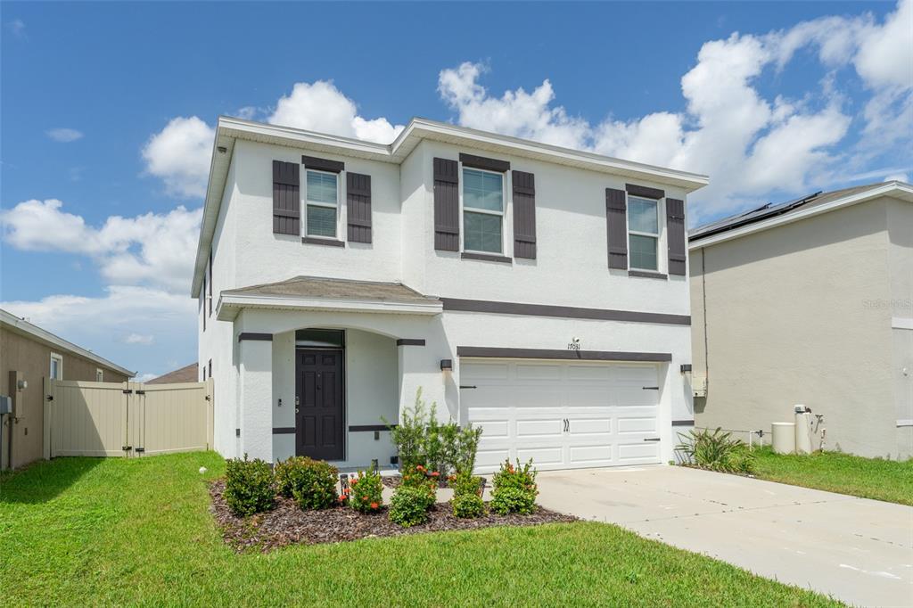 A two-story white house with a two-car garage, dark shutters, and a front porch — 17031 BLISTER WING DRIVE, WIMAUMA, FL