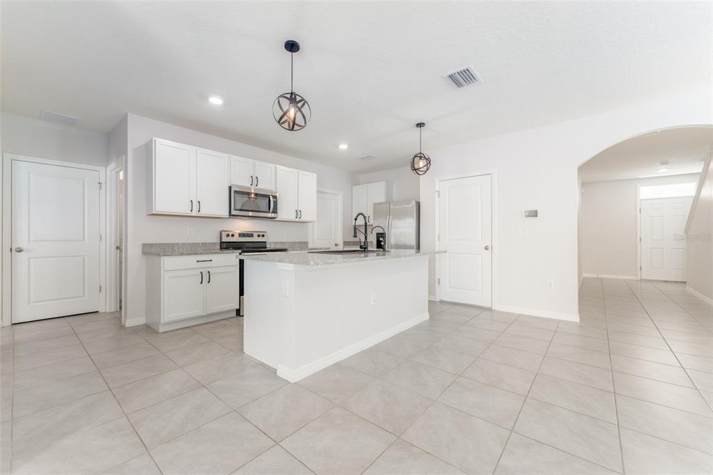 A kitchen with white cabinets, granite countertops, a center island, and light tile flooring — 17031 BLISTER WING DRIVE, WIMAUMA, FL