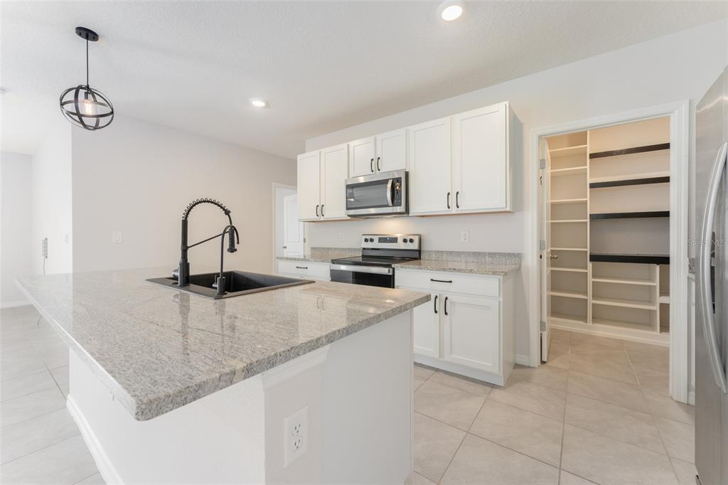 A kitchen with white cabinets, granite countertops, a center island, and an open walk-in pantry — 17031 BLISTER WING DRIVE, WIMAUMA, FL