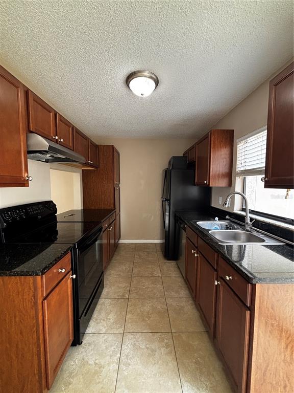 A galley kitchen features wood cabinets, black appliances, dark countertops, and light tile flooring — 1627 LONG RIDGE COURT UNIT 270, ORLANDO, FL