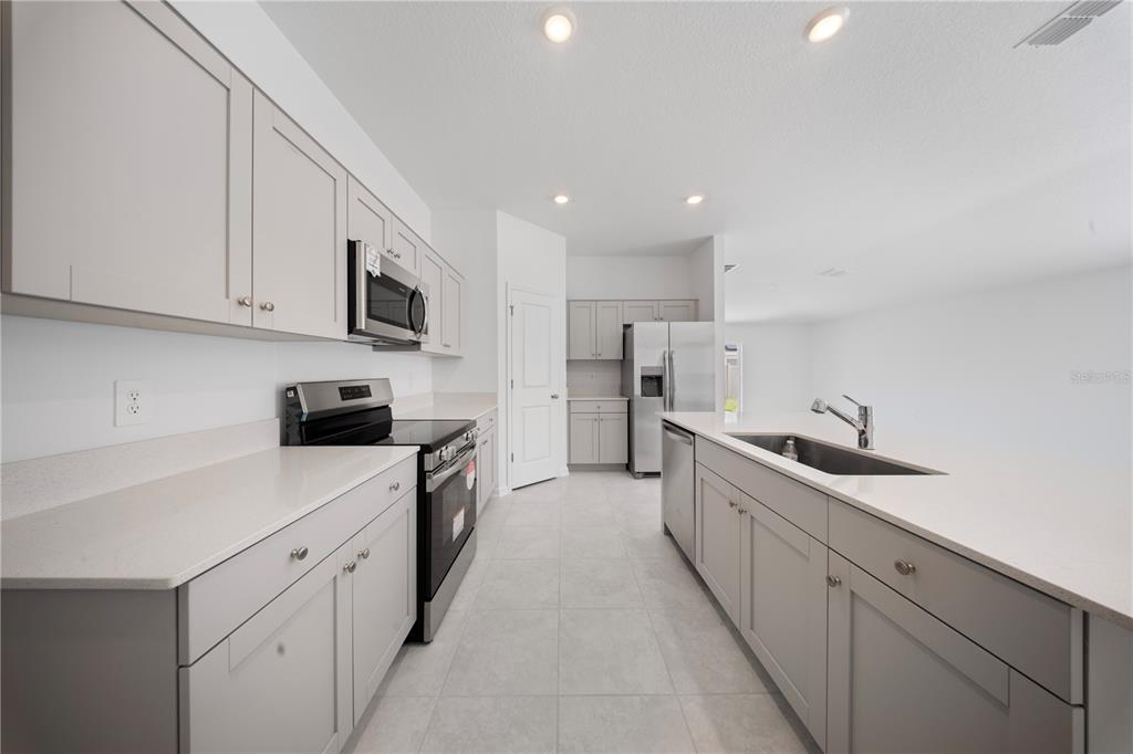 A modern kitchen features light gray cabinets, white countertops, stainless steel appliances, and tile flooring — 501 SEA TURTLE LANE, HAINES CITY, FL