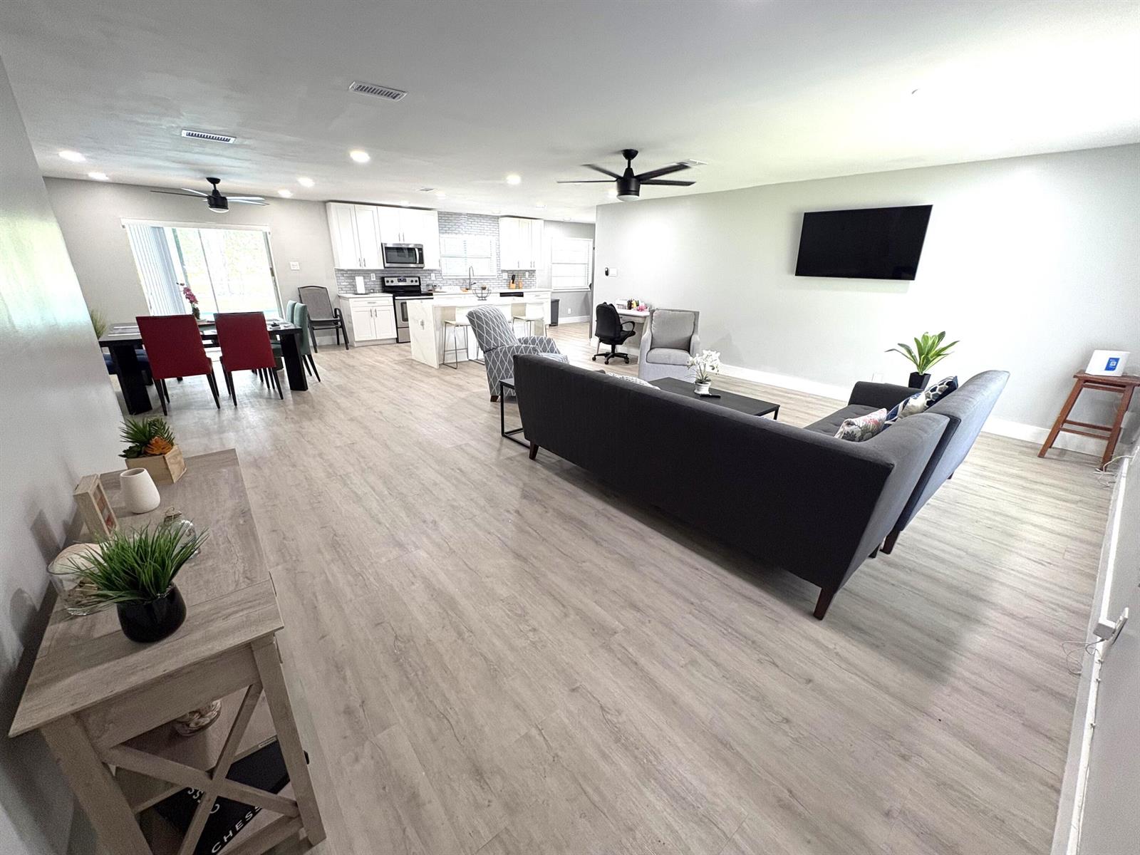 An open-concept living room and kitchen featuring light wood-look flooring and a gray sectional sofa — 1401 NW 75th Terrace, Plantation FL 33313, PLANTATION, FL