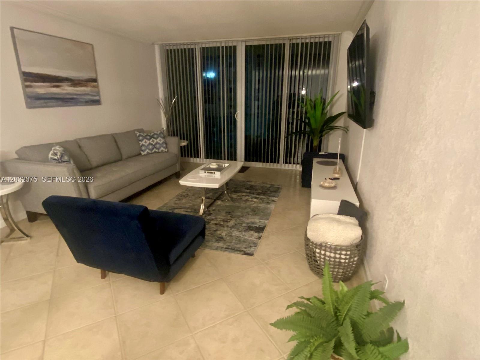 A living room features a gray sofa, blue armchair, white coffee table, and tile floors — 2501 S Ocean Dr, Hollywood FL 33019, HOLLYWOOD, FL