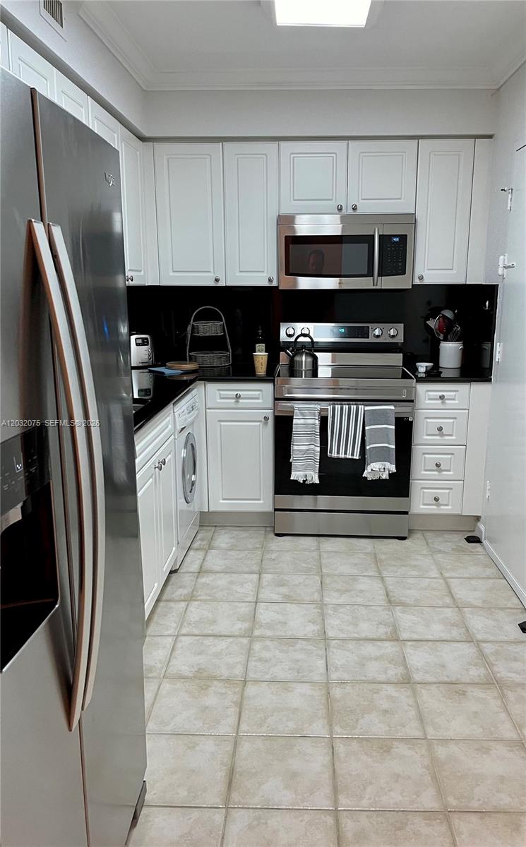 A kitchen features white cabinets, stainless steel appliances, a black backsplash, and tiled flooring — 2501 S Ocean Dr, Hollywood FL 33019, HOLLYWOOD, FL