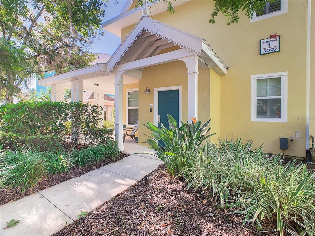 A yellow building exterior features a covered entryway with a teal door and landscaping — 3002 BONFIRE BEACH DRIVE UNIT 202, KISSIMMEE, FL