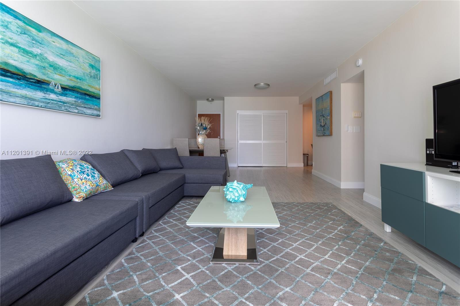 A living room features a gray sectional sofa, a glass coffee table, and a television console — 3901 S Ocean Dr # 10M, Hollywood FL 33019, HOLLYWOOD, FL