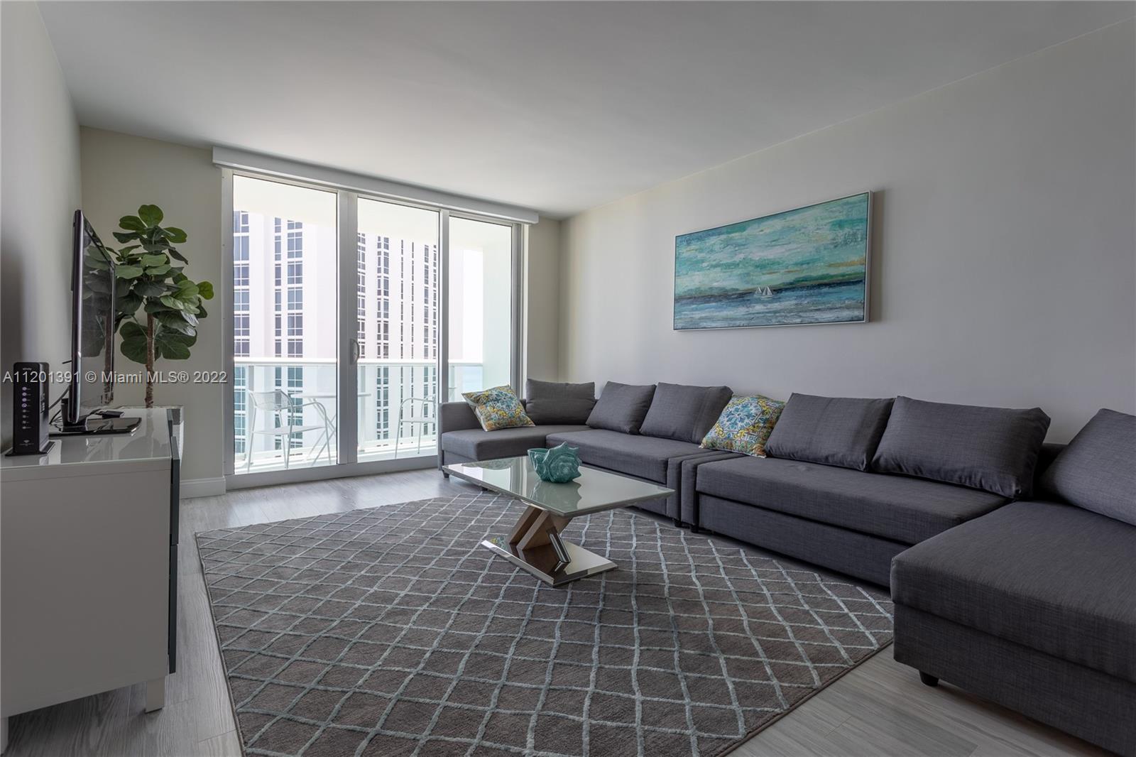 A living room features a gray sectional sofa, a glass coffee table, and a patterned rug — 3901 S Ocean Dr # 10M, Hollywood FL 33019, HOLLYWOOD, FL