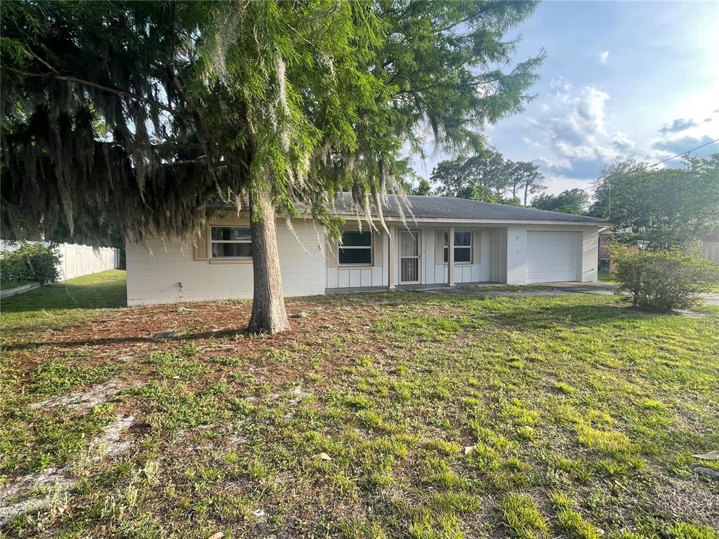 A single-story house with a white exterior, a garage, and a large tree in front — 23 LONESOME PINE TRAIL, YALAHA, FL